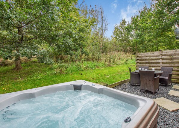 A hot tub surrounded by a wooden fence, outdoor furniture, and lush greenery.