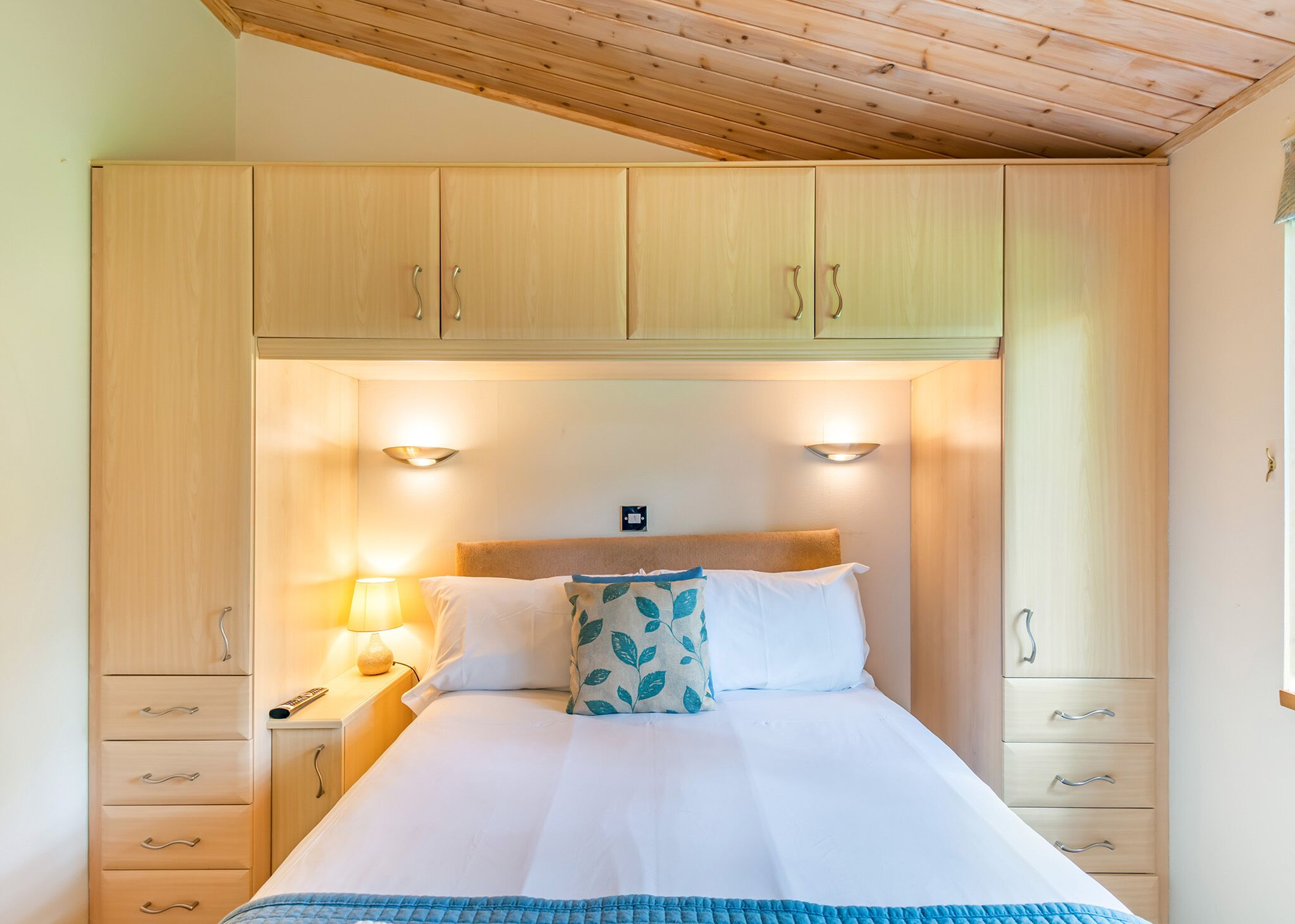 A bedroom with a bed, bedside lamps, a headboard, and wooden cabinets.