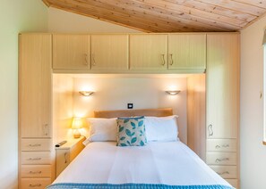 A bedroom with a bed, bedside lamps, a headboard, and wooden cabinets.