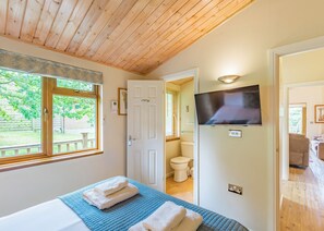 A bedroom with a bed, a TV mounted on the wall, and a window with a view of greenery.