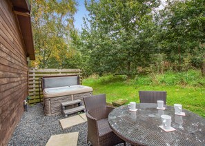 An outdoor patio with a hot tub, wicker chairs, and a glass table with white cups.