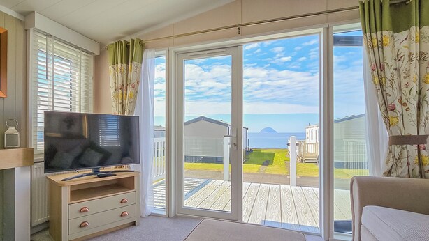 A room with a television, a sofa, and a sliding glass door leading to an outdoor deck. - Modern, contemporary holiday home facing the sea. (Lendalfoot)