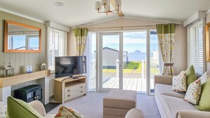 A cozy living room with a television, sofa, and ottoman, a fireplace, and a view of the sea. - Modern, contemporary holiday home facing the sea. (Lendalfoot)