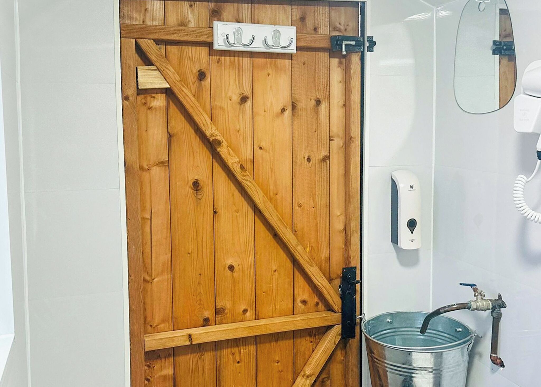 A wooden door with a metal handle, a white wall-mounted phone, and a metal bucket with a faucet.