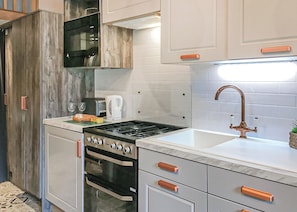 A compact kitchen with a stove, oven, microwave, and a sink with a copper faucet. - Riverside Family Pod HT (Snowdonia)