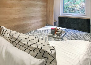 Ein ordentlich bezogenes Bett mit einem Tablett mit Frühstücksgegenständen, ein Fenster mit Blick ins Grüne und ein hölzernes Kopfteil.