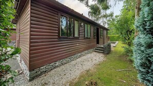 Eine Holzhütte mit Steinuntergrund, großen Fenstern und einem Steinweg, der zum Eingang führt.