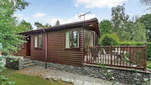 Eine Blockhütte mit Steinuntergrund, einer Holzterrasse und einer Steinmauer, die das Grundstück umgibt.