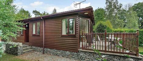 A log cabin with a stone foundation, a wooden deck, and a stone wall surrounding the property.