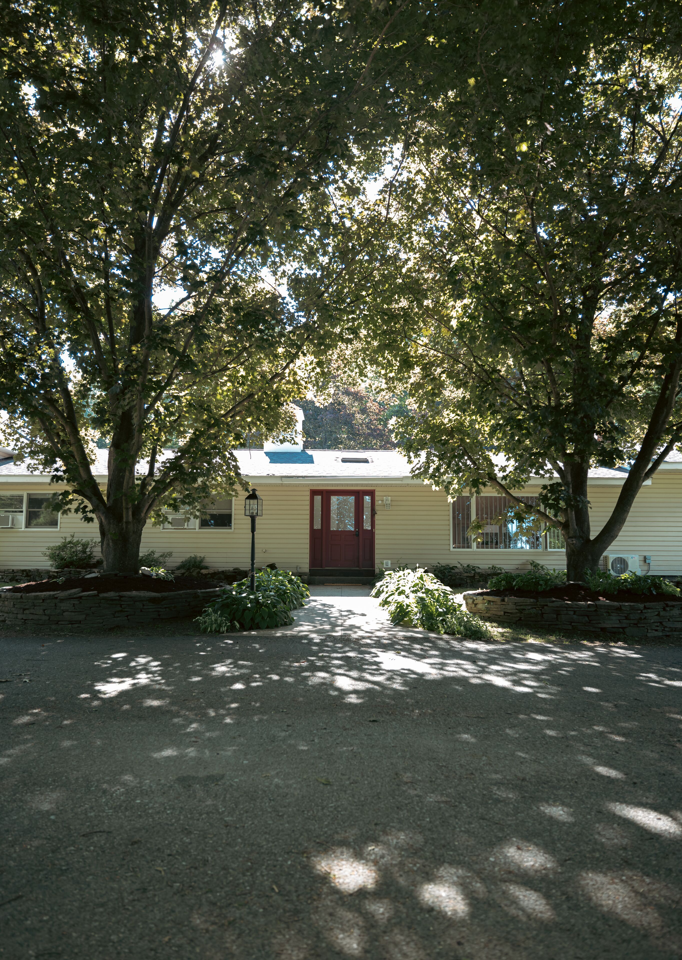 Une maison avec une porte rouge, entourée d’arbres et dotée d’un chemin de pierre menant à l’entrée.