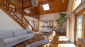 Una habitación amplia con una escalera de madera, una cama con dosel, un sofá blanco y un gran ventanal que deja entrar luz natural.