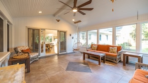 Un espacio habitable amplio con ventilador de techo, muebles de mimbre y ventanas grandes.