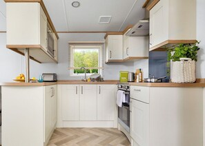 A compact kitchen with white cabinetry, a herringbone-patterned floor, a window with blinds, and a plant on the counter.