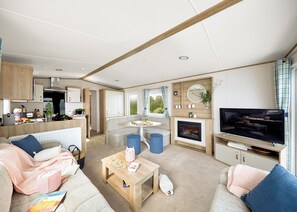 A modern RV interior with a kitchen, dining area, living room, and a TV.