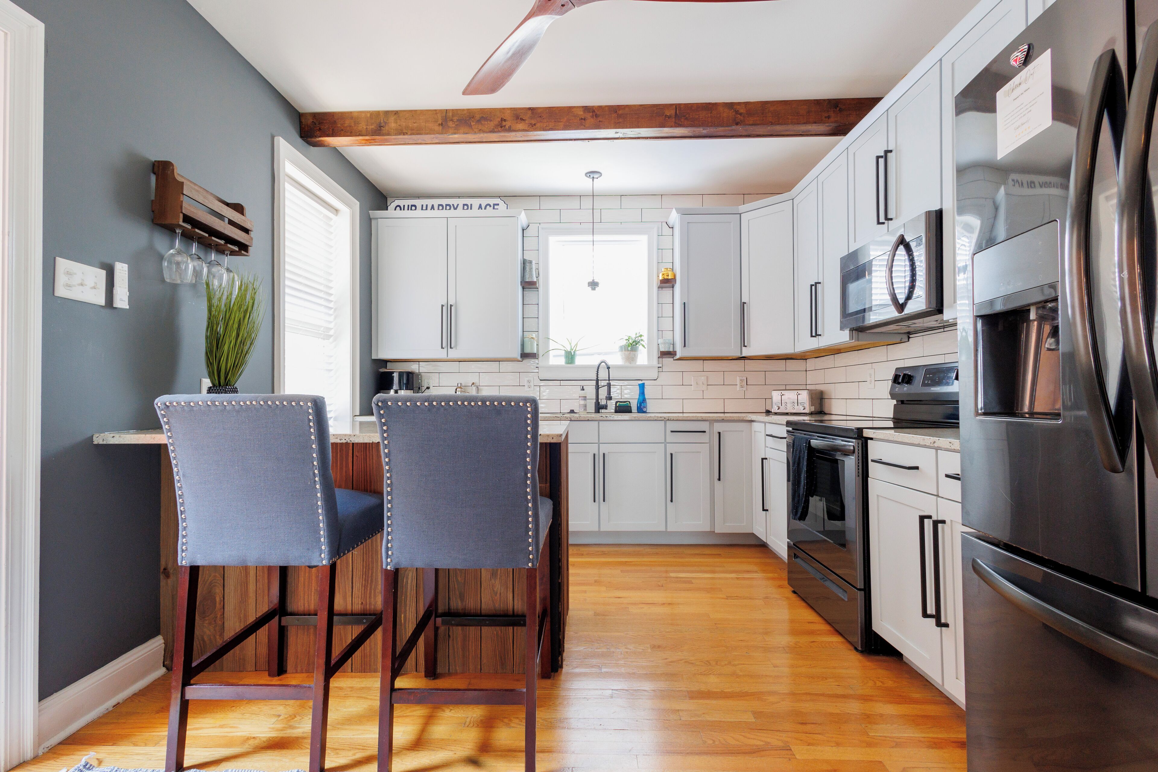 Una cocina moderna con armarios blancos, un refrigerador de acero inoxidable y techo de madera.