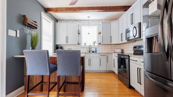 Una cocina moderna con armarios blancos, un refrigerador de acero inoxidable y techo de madera.