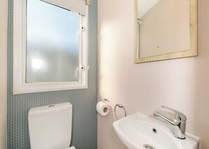 A bathroom with a toilet, sink, mirror, and a window.