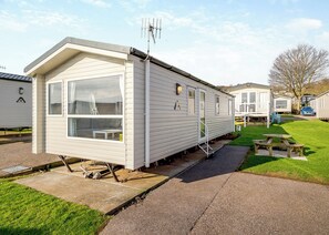 A mobile home with a large window, a small porch, and a picnic table.