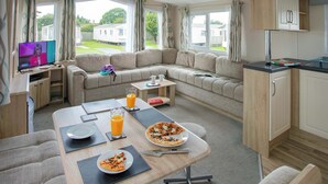 Ein gemütliches Wohnmobil-Interieur mit Esstisch, Sofa, Küchenzeile und einem Fernseher, der eine Nachrichtensendung zeigt.