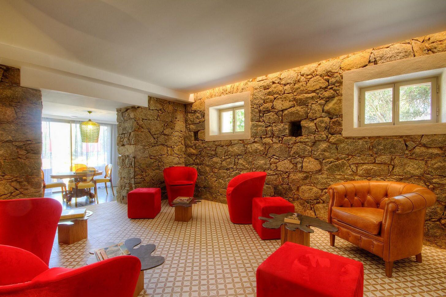 A room with a stone wall, red chairs, a leather sofa, and a tiled floor.
