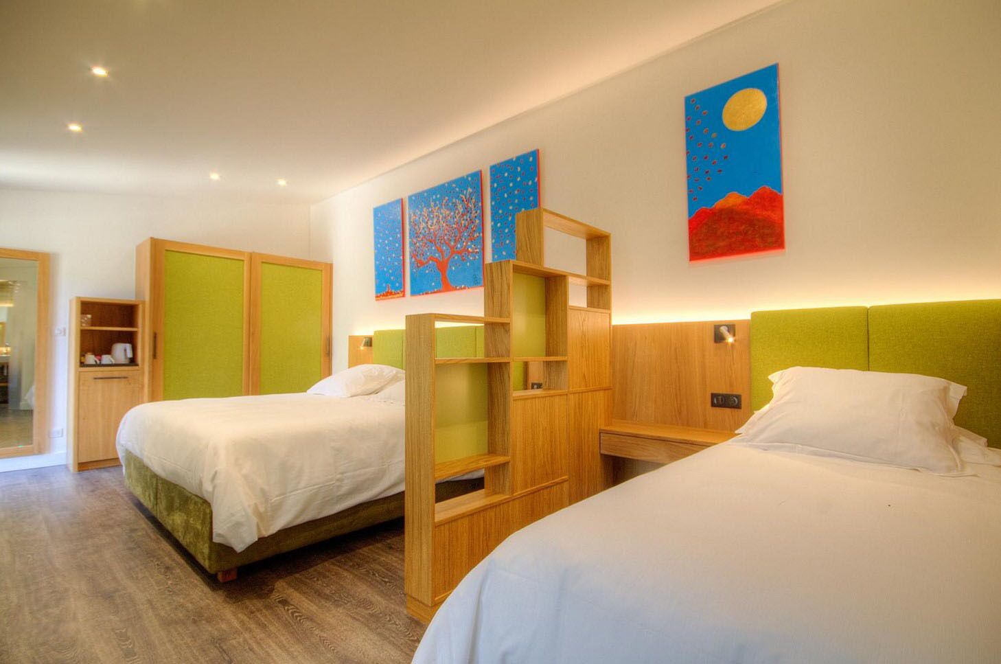 Ein Hotelzimmer mit zwei Betten, einem Holzschrank, einem kleinen Schreibtisch und Bildern an der Wand.