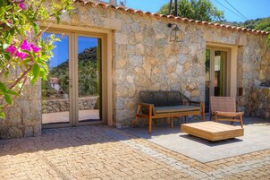 Un edificio de piedra con techo de tejas, un banco de madera, una mesa de madera y una silla de mimbre.