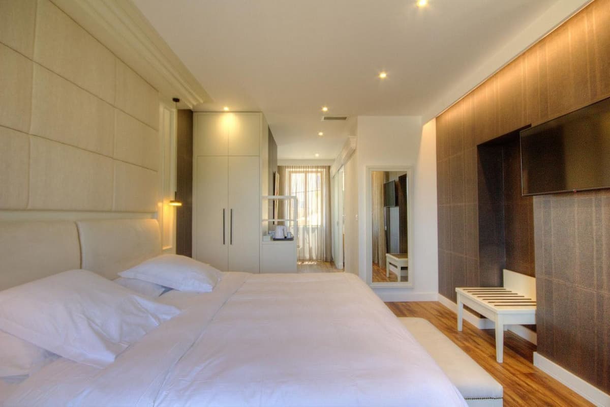 A modern hotel room with a large bed, a seating area, a TV, and a wardrobe.