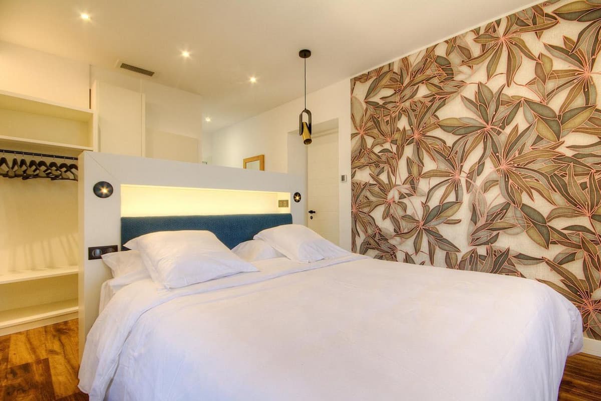 A hotel room with a bed, a wardrobe, and a wall with a leaf pattern.