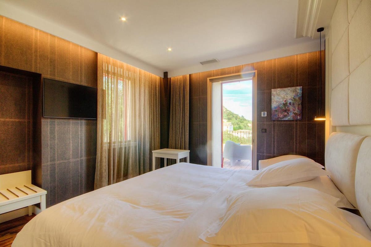 A modern hotel room with a large bed, a small table, and a view of the outdoors.