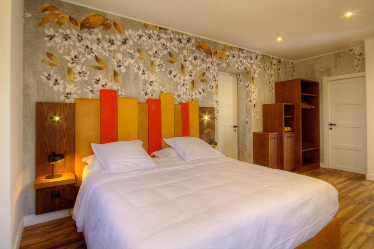 A bedroom with a bed, a nightstand, a wardrobe, and a floral-patterned wall.