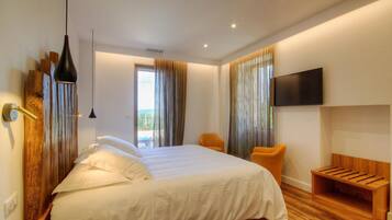 Habitación de hotel moderna con una cama grande, un banco de madera, un televisor montado en la pared y un balcón con cortinas.