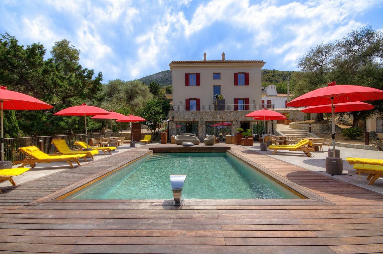 Un espace piscine doté d’une terrasse en bois, de chaises longues jaunes et de parasols rouges.
