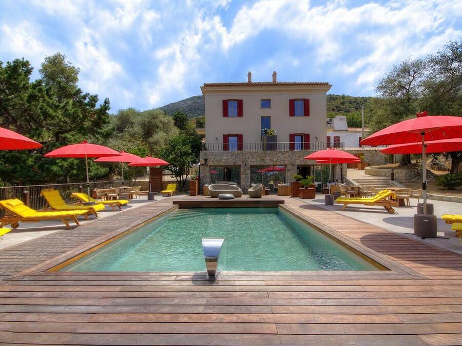 Un espace piscine doté d’une terrasse en bois, de chaises longues jaunes et de parasols rouges.