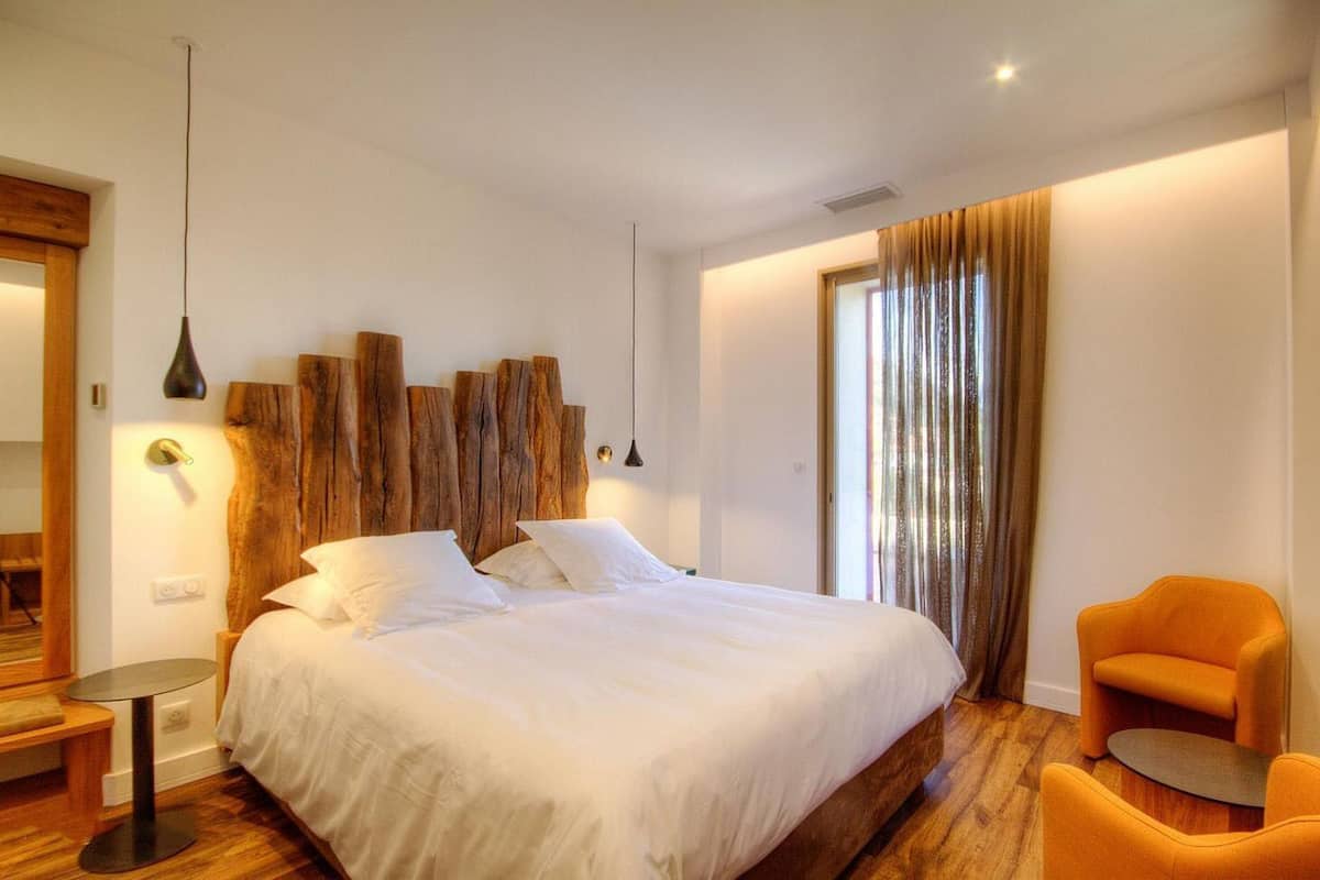 A bedroom with a large bed, a round side table, an orange chair, and a wooden headboard.