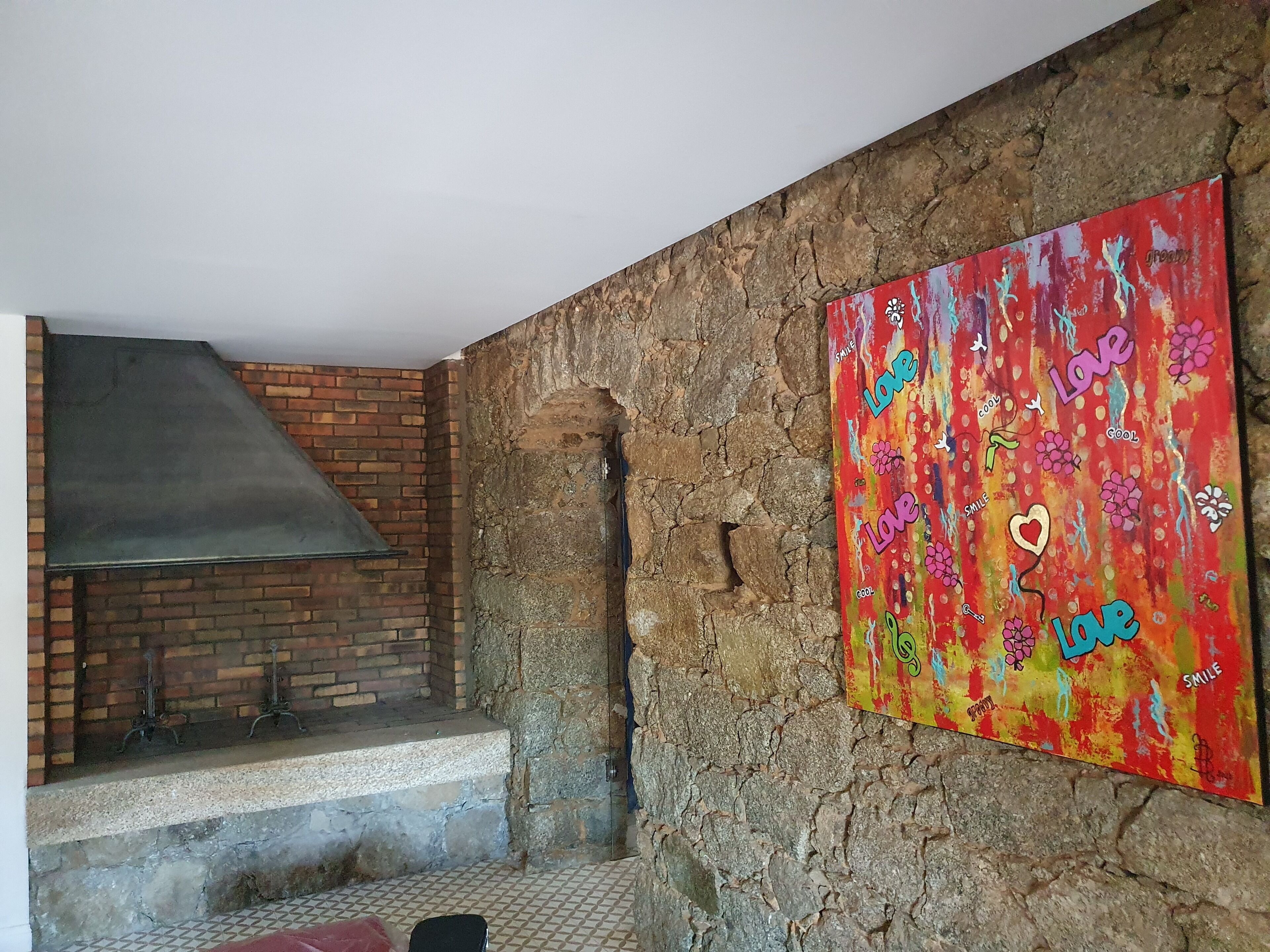 Ein rustikaler Innenraum mit Kamin aus Ziegelsteinen, einer Steinwand und einem farbenfrohen abstrakten Gemälde.