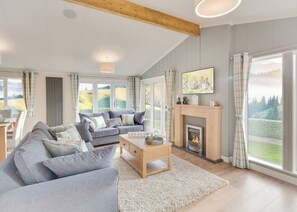 A spacious living room with a fireplace, a sofa set, and large windows offering a view of the outdoors.