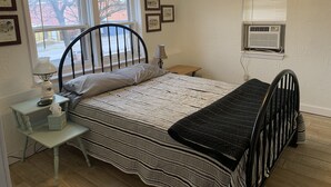 Un dormitorio con cama, mesita de noche, lámpara y ventana.