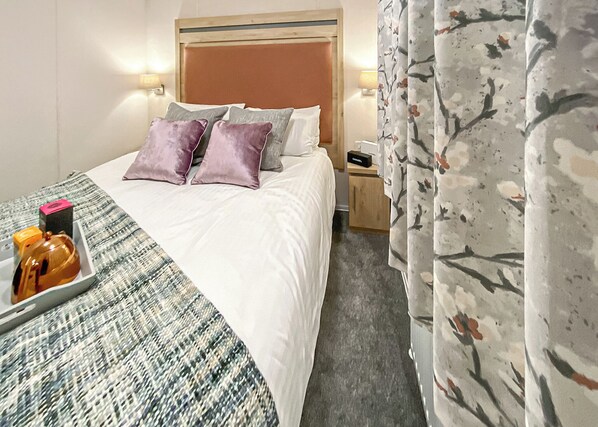 A hotel room with a bed, pillows, a nightstand, a lamp, a tray with items, and a floral curtain. - 2 bedroom accommodation in Snowdonia (Snowdonia)