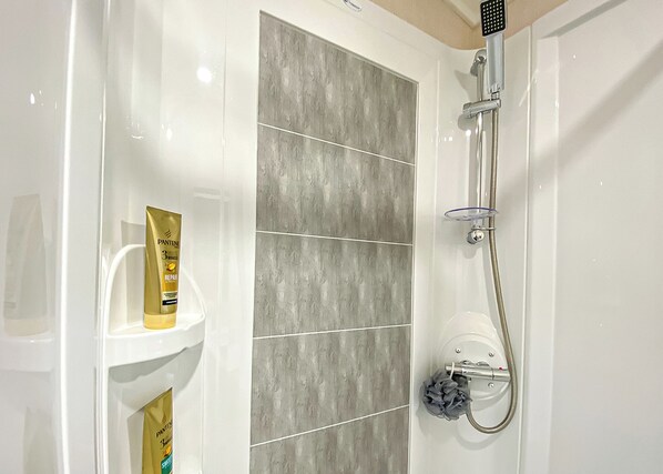 Ein Badezimmer mit Dusche, einem weißen Waschbecken und einer Pantene-Shampoo-Flasche.