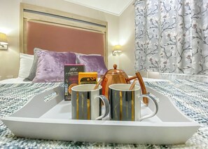 Quarto de hotel com cama, almofadas, bandeja com canecas, bule e uma caixa de chá Twinings.