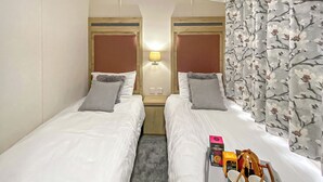 A hotel room with two single beds, a nightstand with a lamp, a small table with breakfast items, and floral curtains. - 2 bedroom accommodation in Snowdonia (Snowdonia)