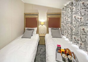 Ein Hotelzimmer mit zwei Einzelbetten, einem Nachttisch mit Lampe, einem kleinen Tisch mit Frühstücksangeboten und blumigem Vorhang.