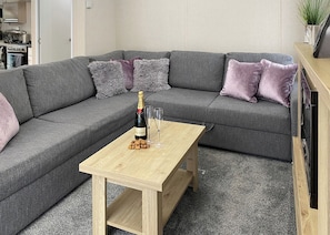 Een grijze modulaire bank met kussens, een houten salontafel en een fles champagne.