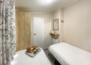 Ein Hotelzimmer mit einem Bett, einem Nachttisch mit Tablett, einem Holzschrank, einer weißen Tür, einem kleinen Waschbecken mit Spiegel und einem Heizkörper.