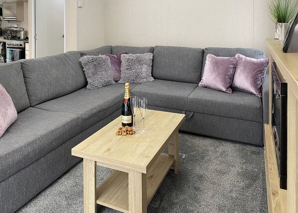 Un canapé d’angle gris avec des coussins, une table basse en bois et une bouteille de champagne.