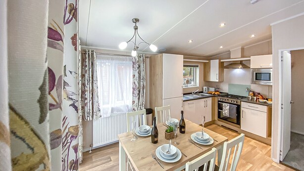 A modern kitchen with a dining table set for two, a stove, oven, and a microwave. - 2 bedroom accommodation in Snowdonia (Snowdonia)