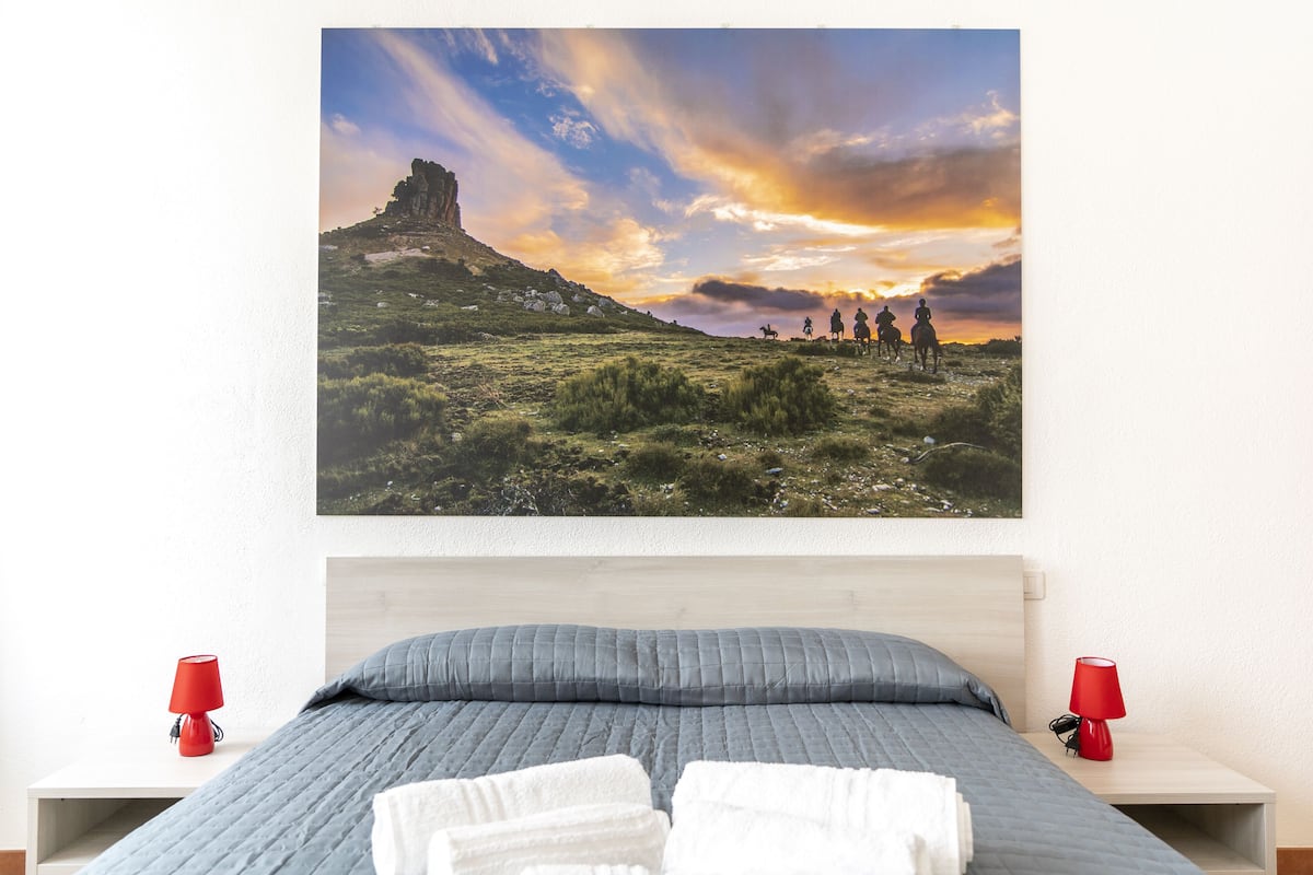 A bedroom with a bed, two bedside tables, and a large landscape painting on the wall.