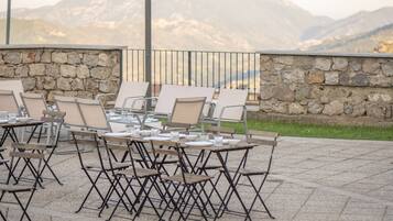 An outdoor patio with tables and chairs, stone walls, and a mountain view.
