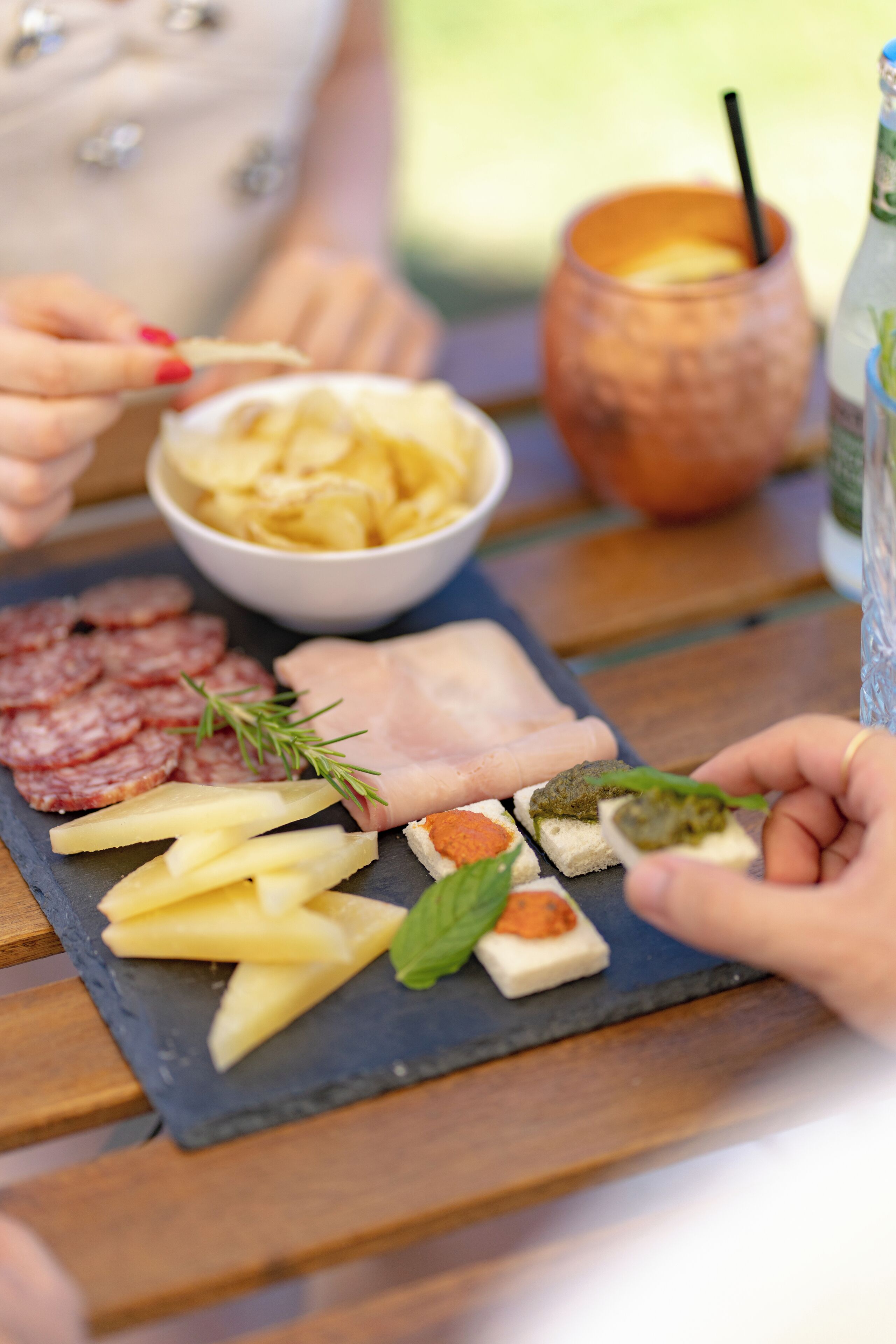 A charcuterie board with various meats, cheeses, and vegetables on a slate board.