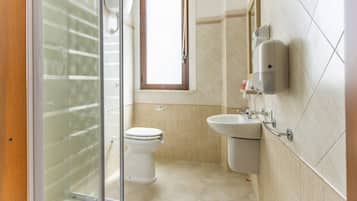 A bathroom with a glass shower enclosure, a toilet, a sink, and a mirror.